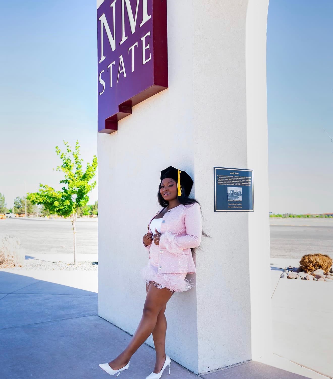 Graduate posing by the NM State sign