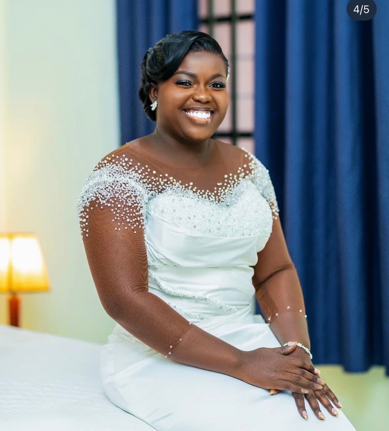 Bride in a beaded gown against a blue curtain